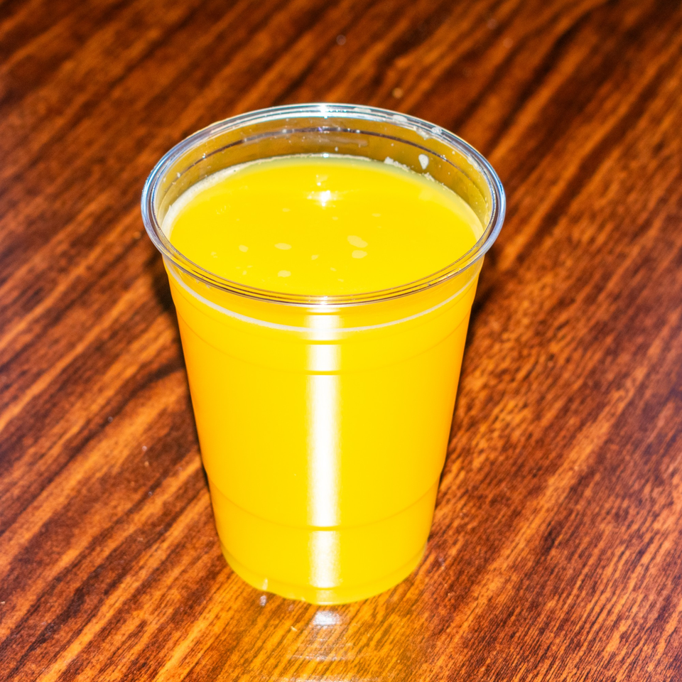 A clear plastic cup filled with bright yellow orange juice sits on a wooden table.