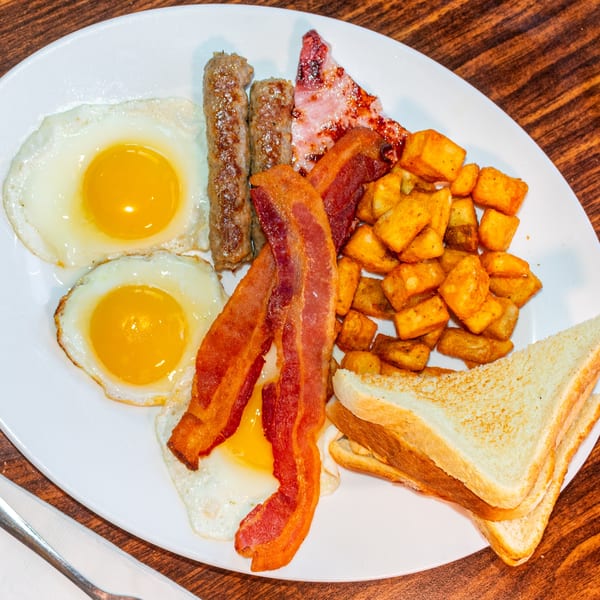 A J's Brothers breakfast plate with fried eggs, bacon, sausage, home fries, and toast.