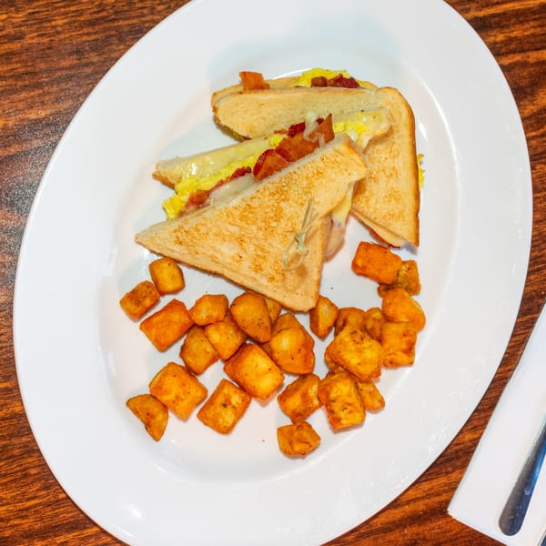 J's Brothers breakfast sandwich with bacon, egg, and cheese, served with crispy hash browns.