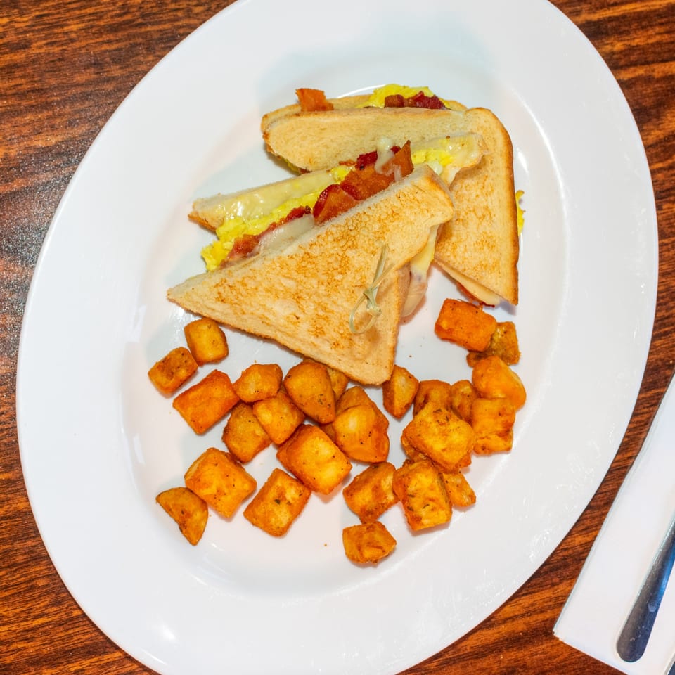 J's Brothers breakfast sandwich with bacon, egg, and cheese, served with crispy hash browns.