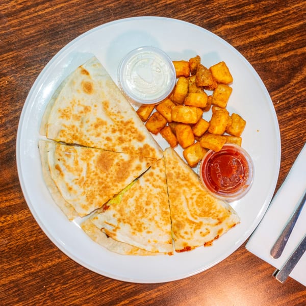 A breakfast quesadilla cut into four triangles, served with crispy potato tots, salsa, and sour cream.