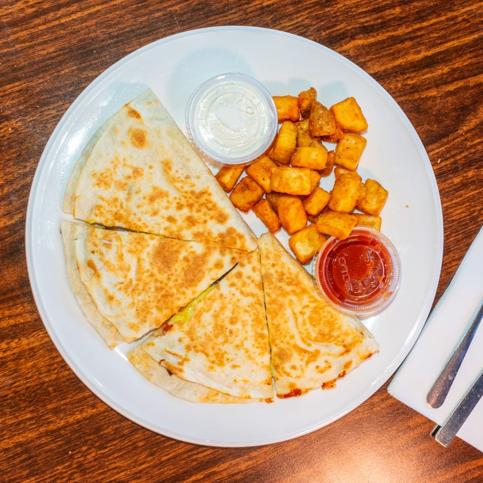A breakfast quesadilla cut into four triangles, served with crispy potato tots, salsa, and sour cream.