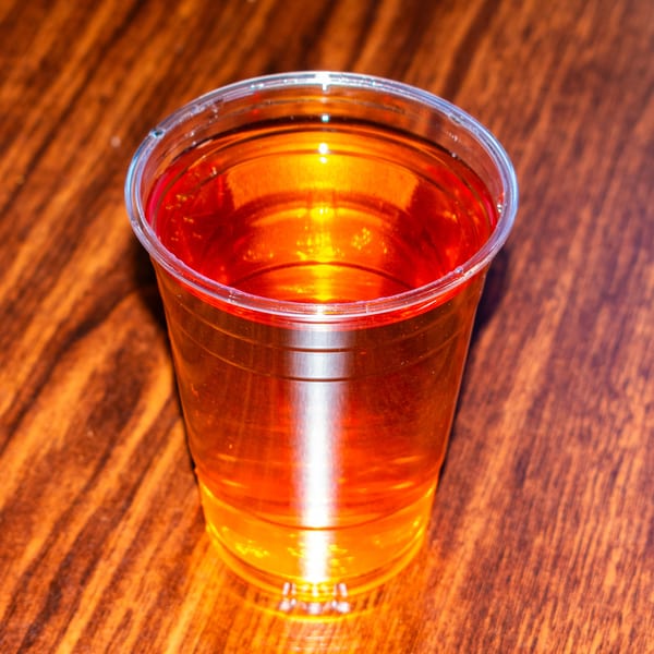 A clear plastic cup filled with a golden-orange beverage sits on a wooden table.