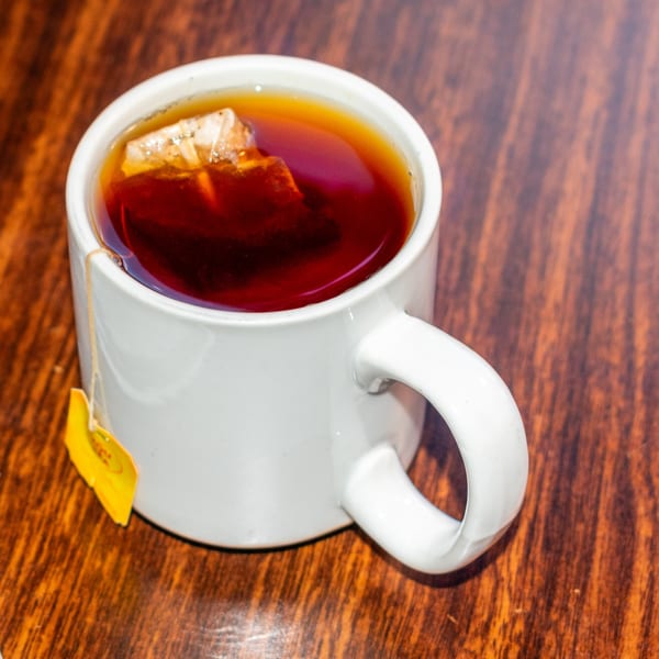 A white mug filled with dark tea and a tea bag steeping on a wooden table.